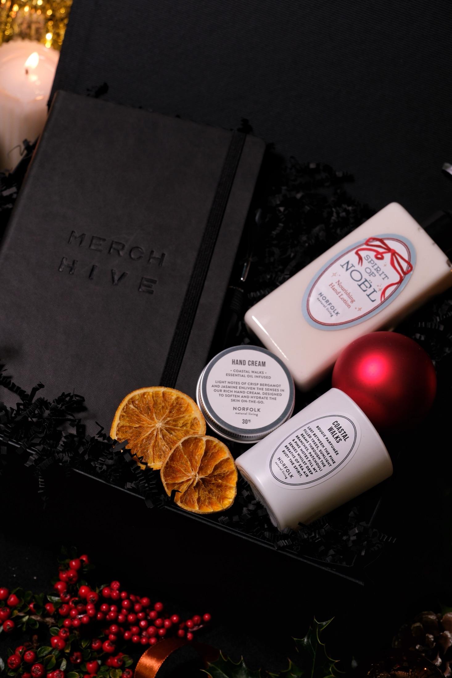 Black debossed Merch Hive notebook with hand cream and lotion, dried orange slices and a red bauble